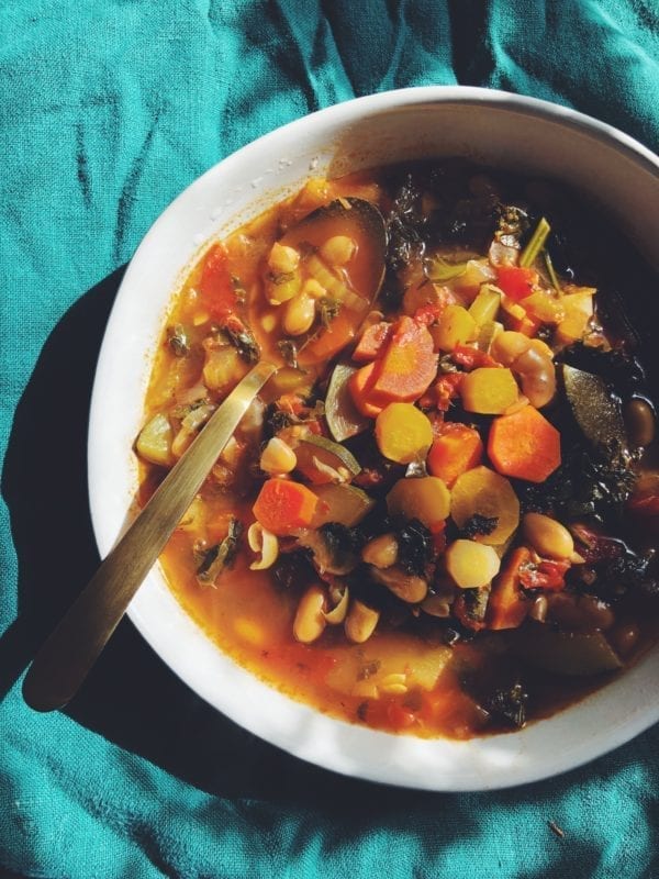 Spicy Lemon, Kale and White Bean Detox Soup in a white bowl on a green tablecloth