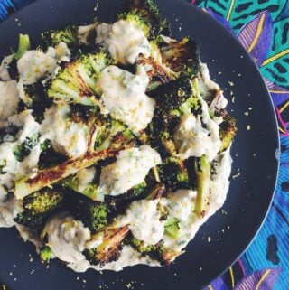 Roasted Broccoli with Lemon Herb + Garlic Tahini Sauce on a black plate