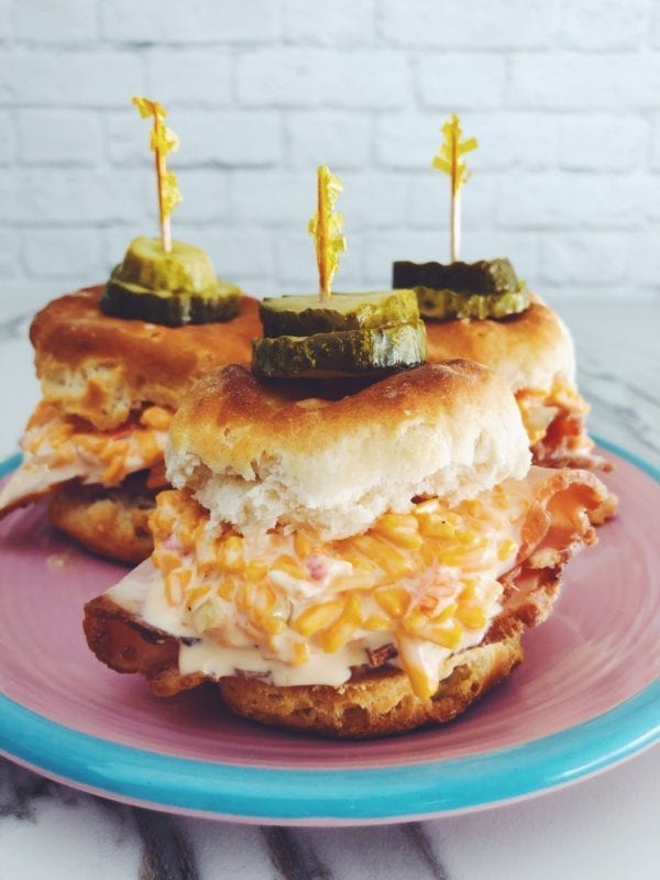 three pimento cheese biscuit sliders on a pink and blue plate with a white background