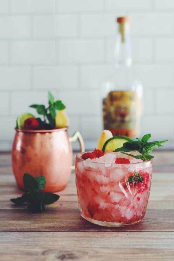 Two pink cocktails on a wooden table with white subway tile in the background