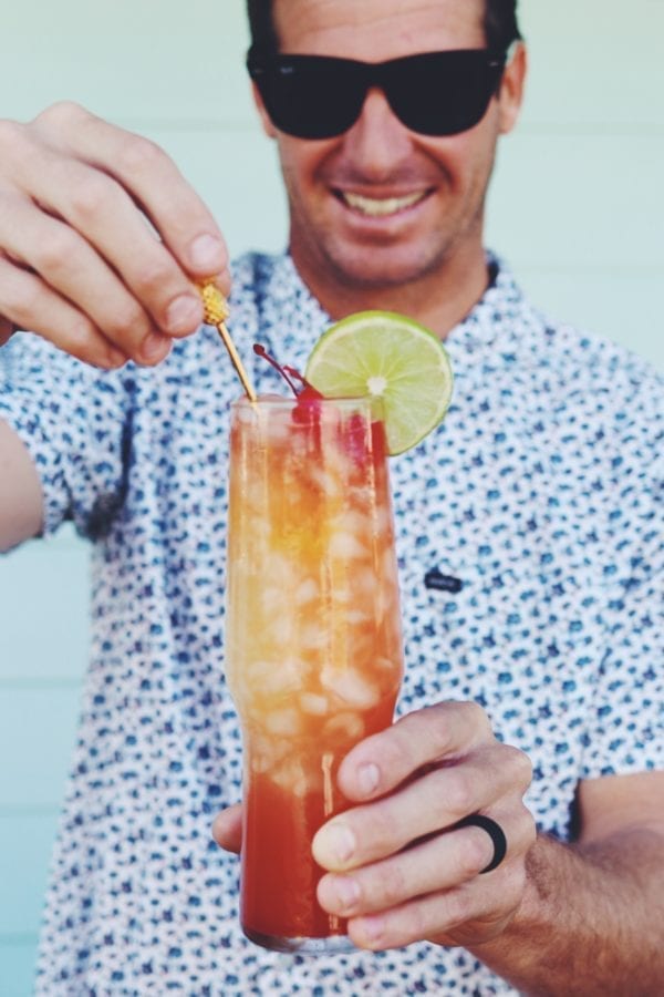 Jeremy Johnston wearing a floral shirt against a blue background holding a orange and red punch cup with a lime on it