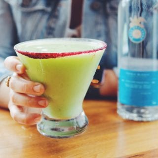 a hand holding a bright green avocado margarita at disney springs