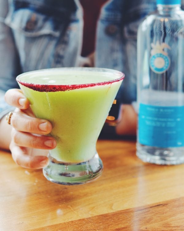 a hand holding a bright green avocado margarita at disney springs