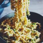 a fork holding up mafalda pasta in a green bowl with bits of of broccoli, lemon zest , garlic and red pepper flakes