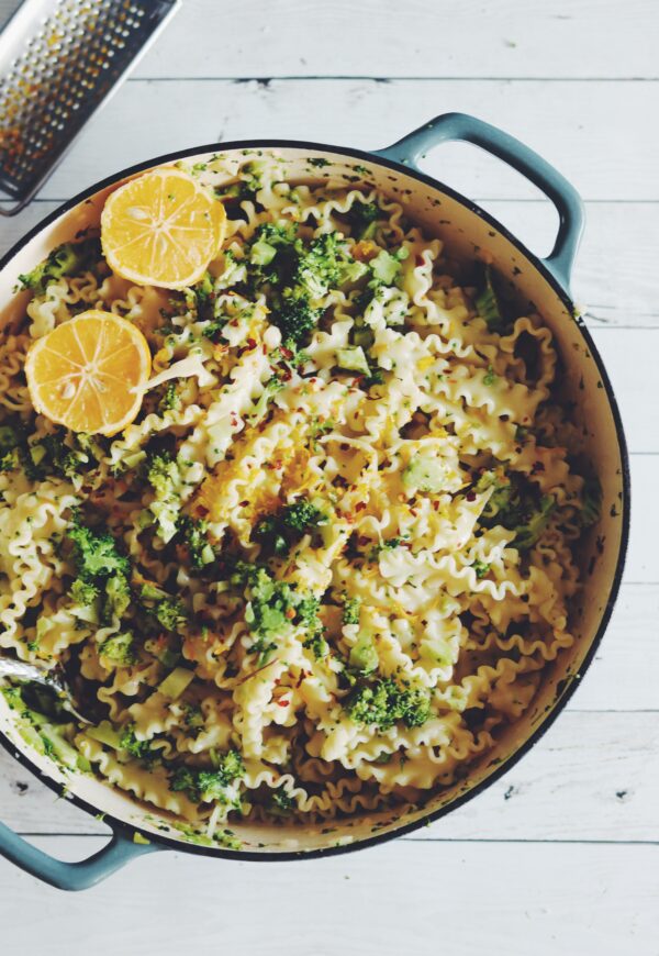 malfada pasta with broccoli, red pepper flakes and yellow lemon zest in a blue pan over a white wooden table