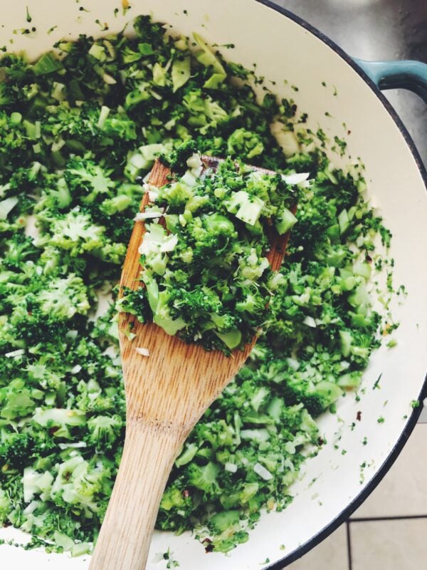 chopped broccoli with garlic in a pan with a wooden spoon