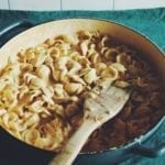 overhead shot of ear-shaped pasta covered in orange cream sauce with a blue background and a wooden spatula