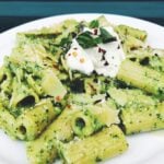 bright green pesto pasta with a spoonful of white ricotta on top