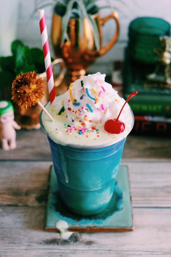 a shiny aqua cup filled with a green milkshake with rainbow sprinkles, whipped cream and a cherry on top