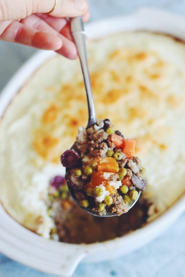 a white ceramic bowl filled with baked mashed cauliflower with a spoon scooping up a mixture of colorful vegetables and ground meet