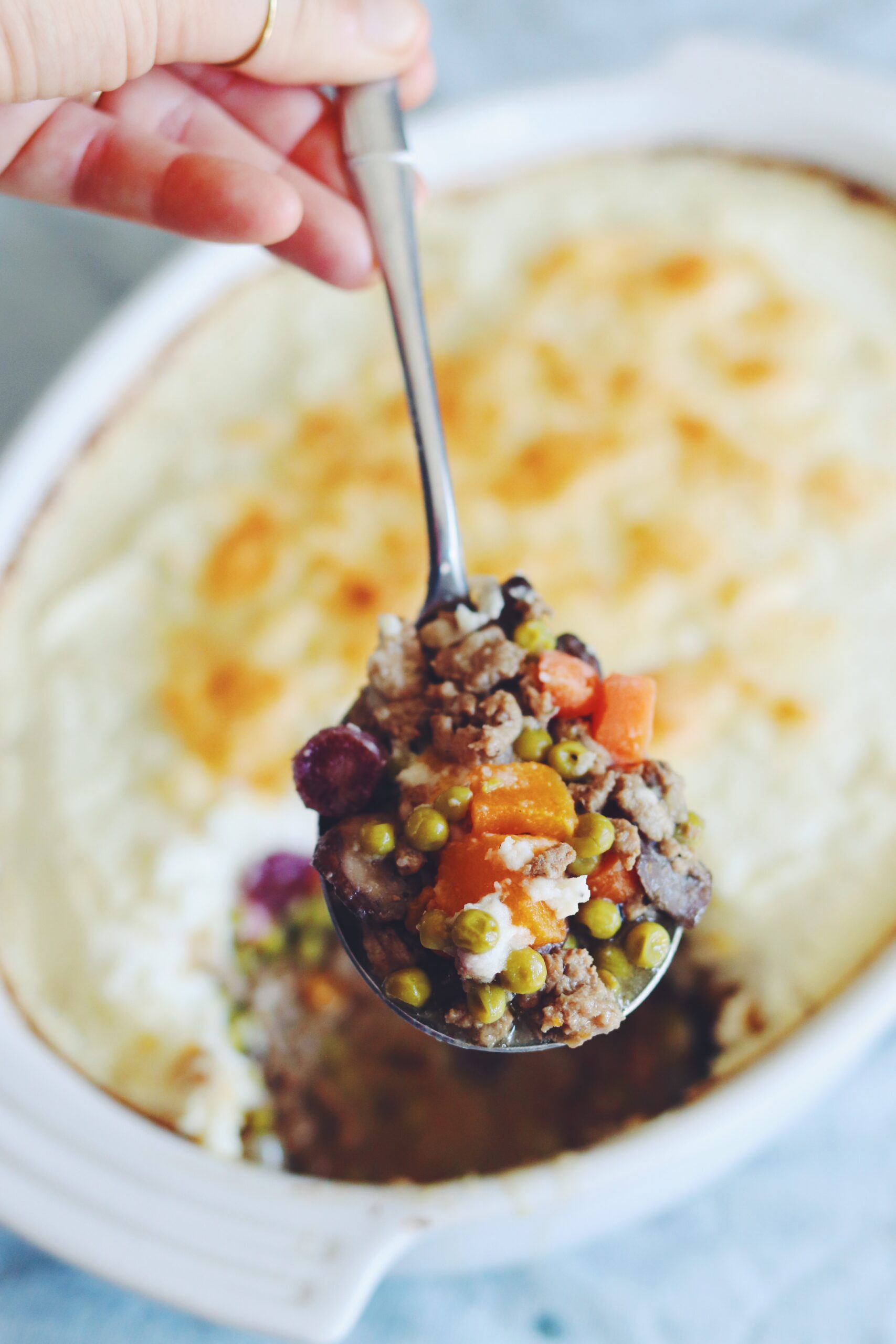 a white ceramic bowl filled with baked mashed cauliflower with a spoon scooping up a mixture of colorful vegetables and ground meet