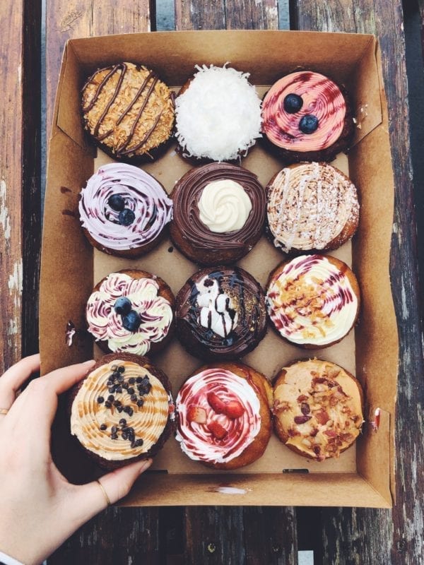 colorful donuts in a box with a hand reaching for them 