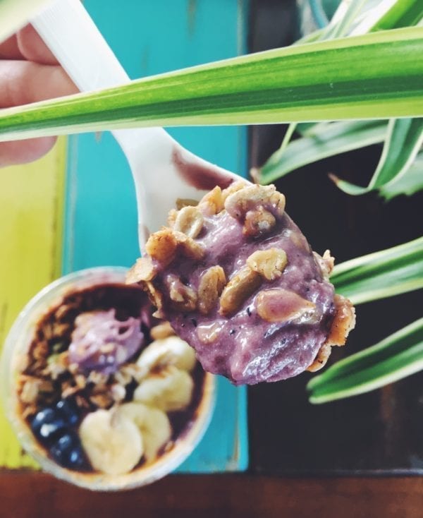 a spoon scooping up some purple acai with granola in it on a blue background