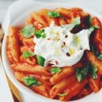 a bowl of penne pomodoro with burrata and basil on top