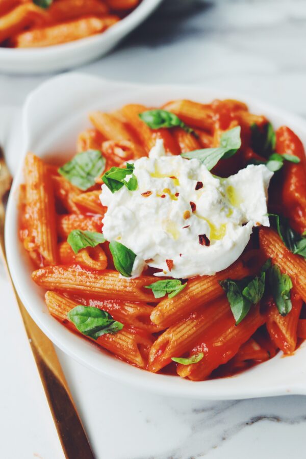 a bowl of penne pomodoro with burrata and basil on top