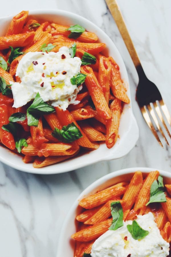 two bowls of penne pomodoro with burrata and basil on top