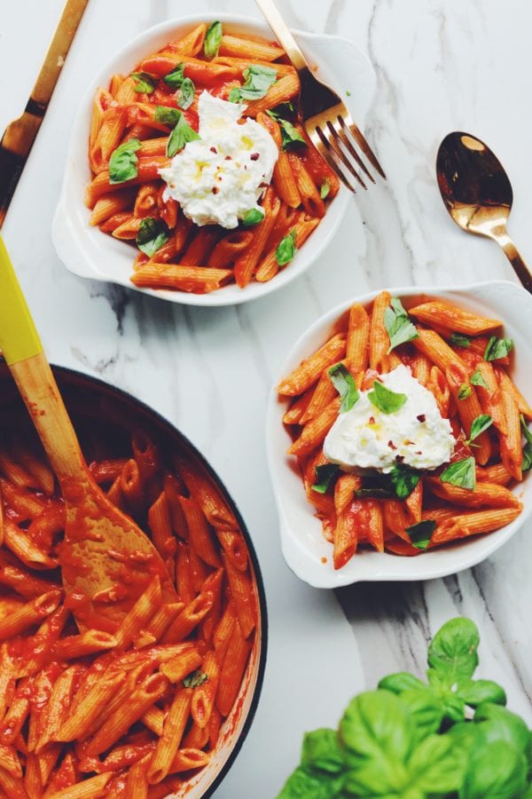two bowls of penne pomodoro with burrata and basil on top