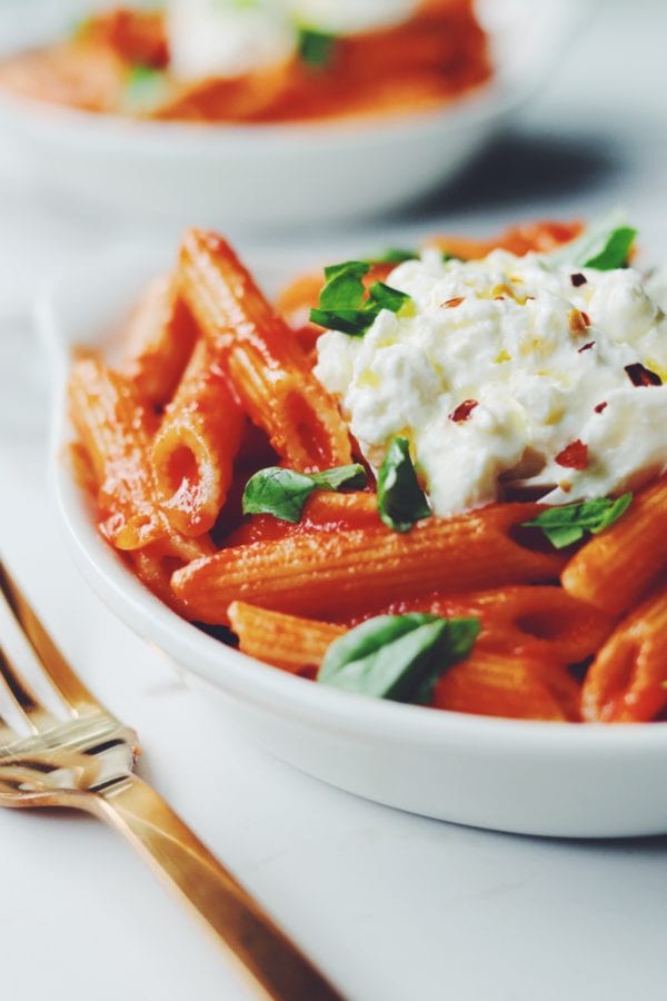 a bowl of penne pomodoro with burrata and basil on top