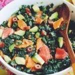 kale salad with chunks of citrus in a white bowl