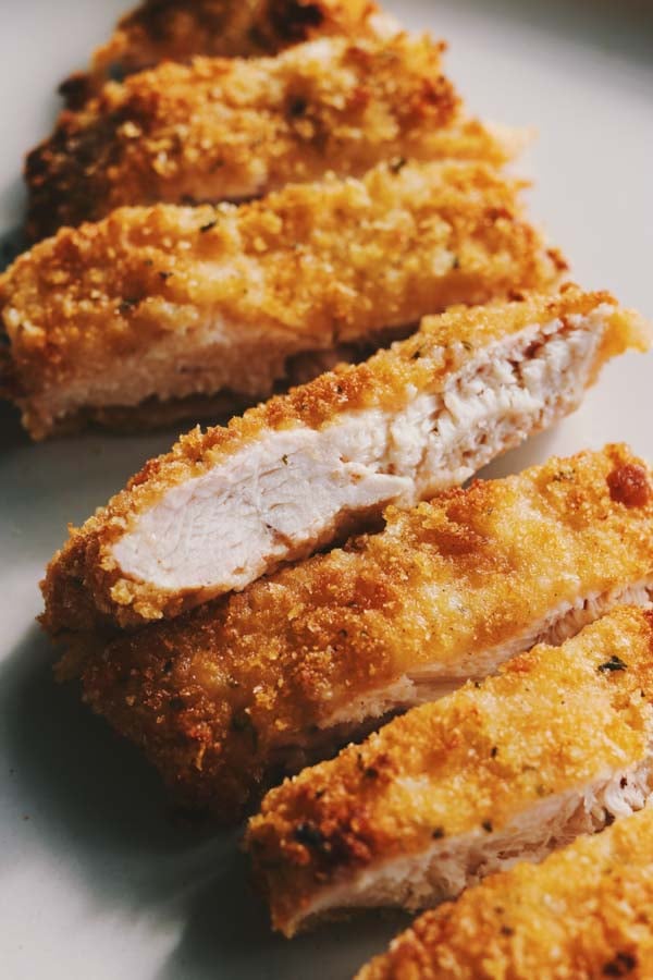 a piece of crispy chicken cutlet cut into pieces - showing the juicy white meat interior.