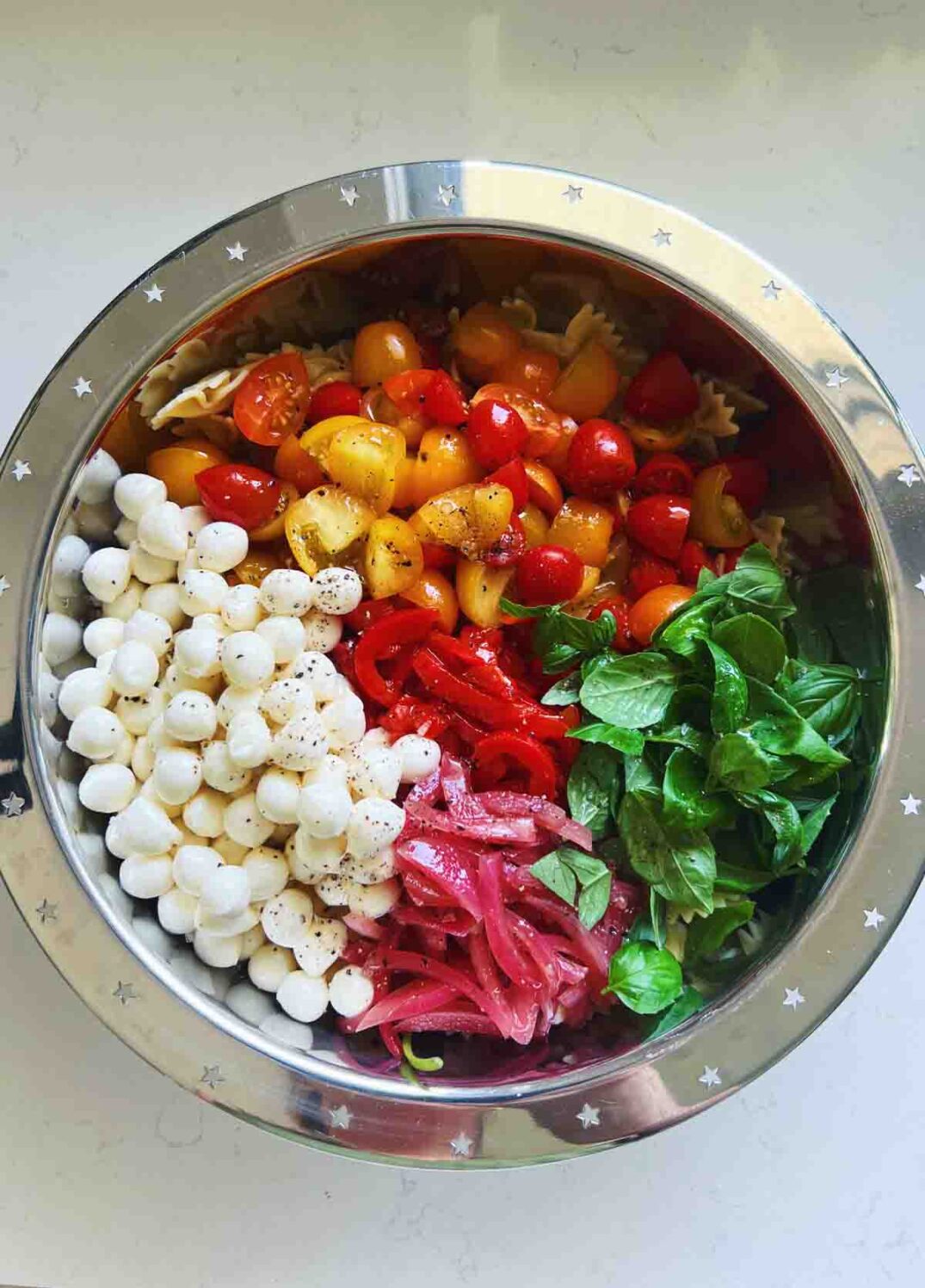 deconstructed caprese pasta salad in a silver bowl on a white countertop.