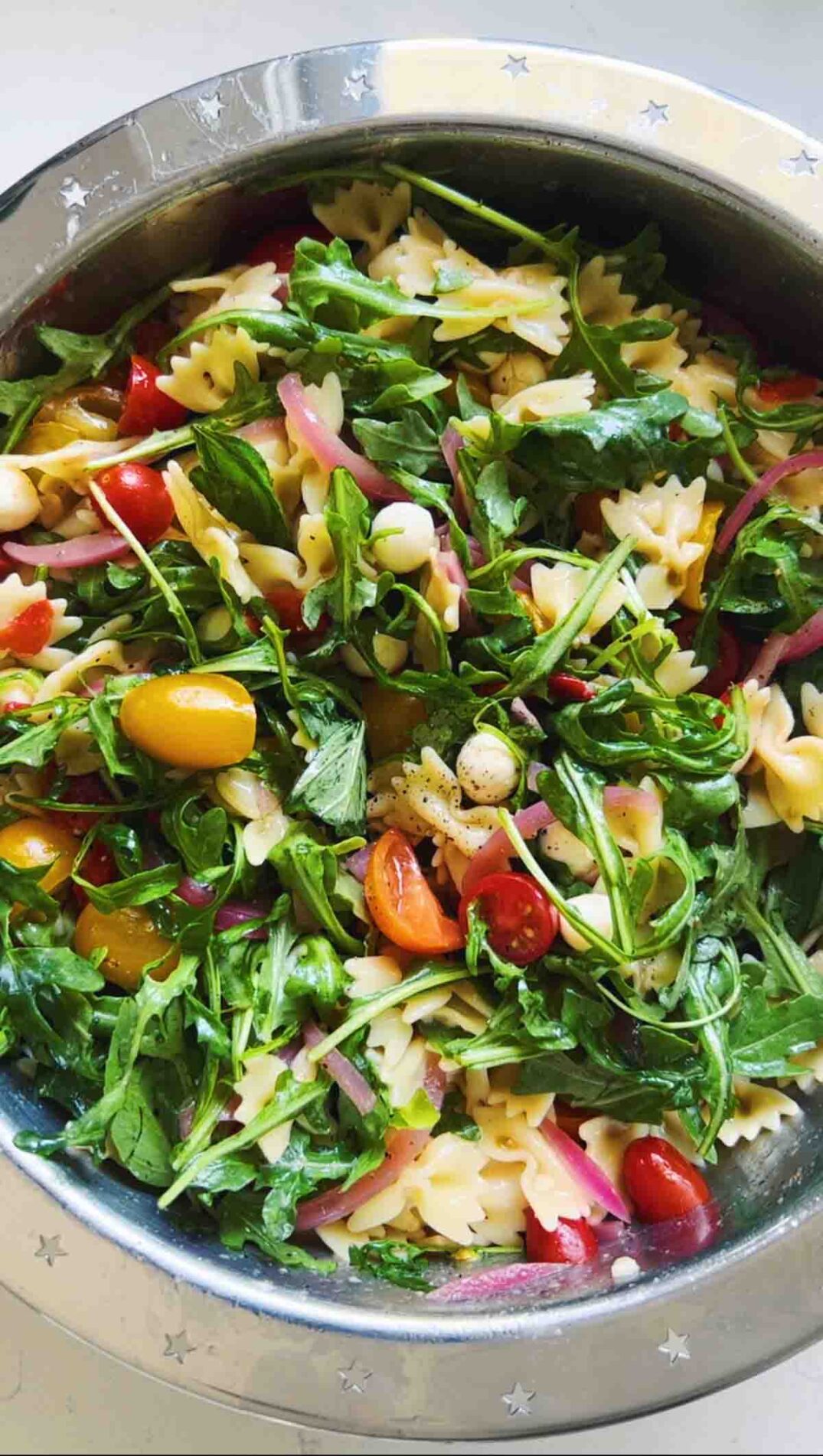 arugula and pasta salad ingredients in a big silver bowl.