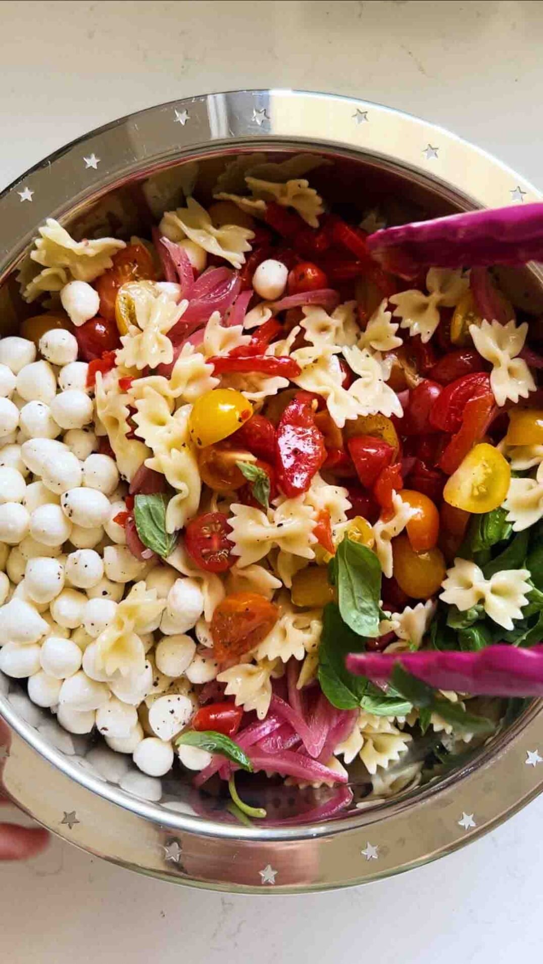 pink tongs tossing together caprese pasta salad.