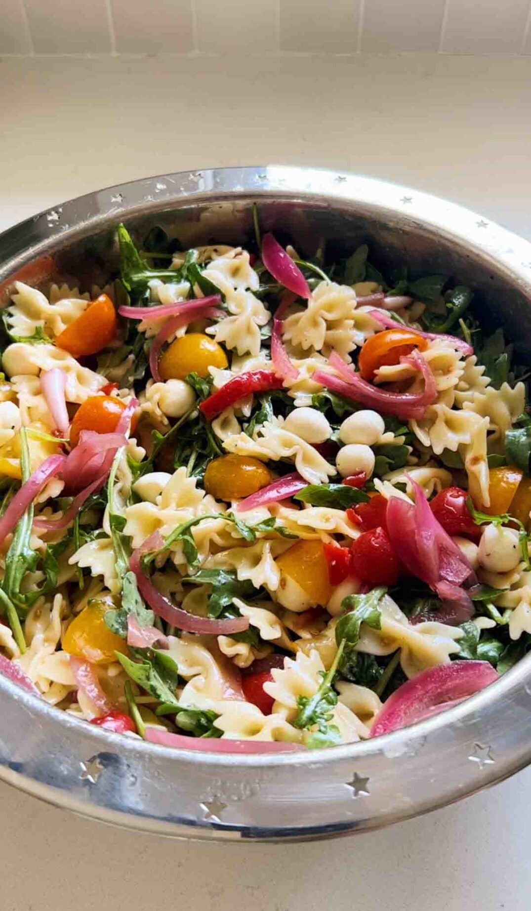 caprese pasta salad in a silver bowl sitting on a white countertop.