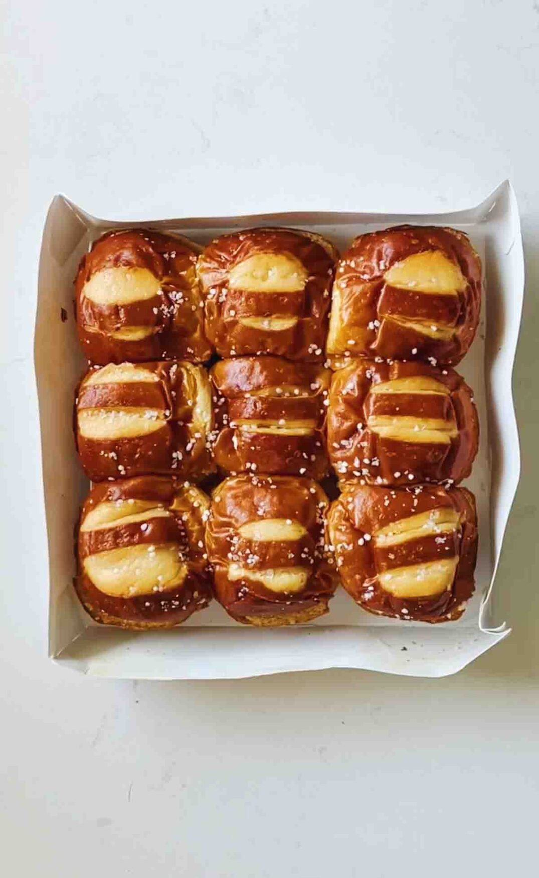 pretzel buns in a white box on a white countertop.