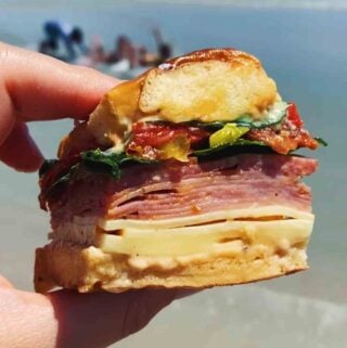 a hand holding an italian slider with the beach in the background.