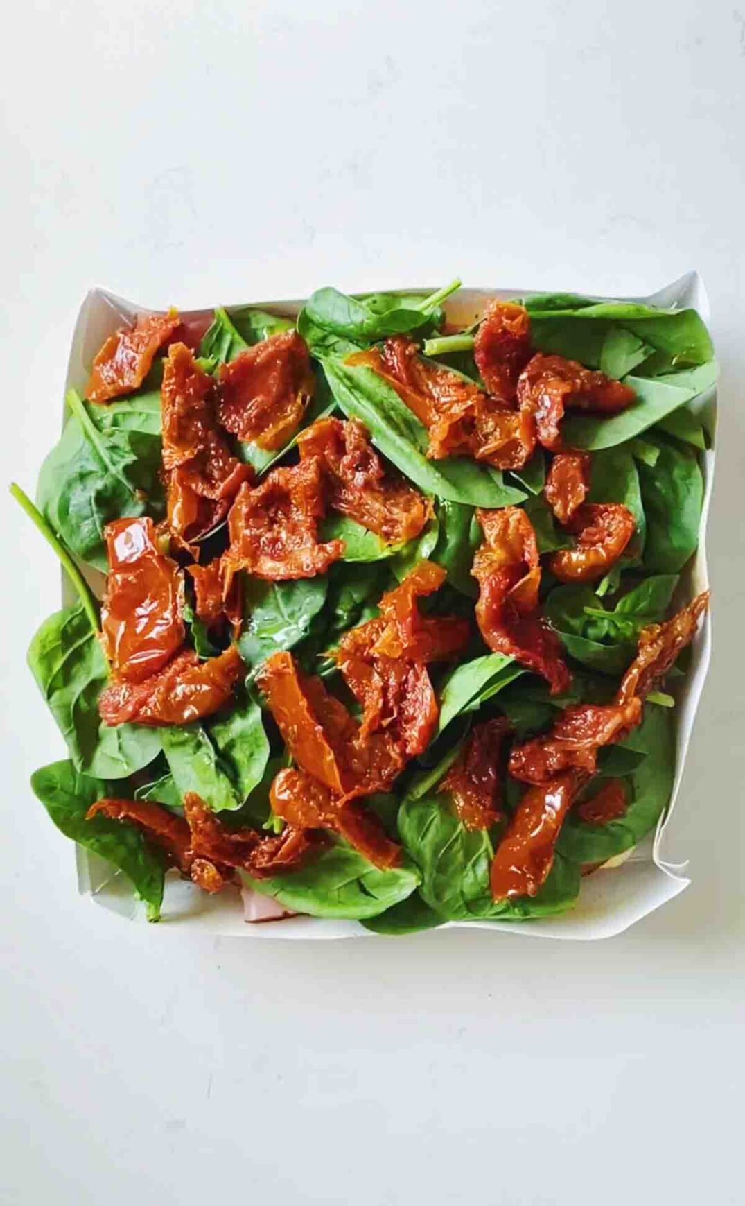 fresh spinach and sun dried tomatoes on top of a white countertop.