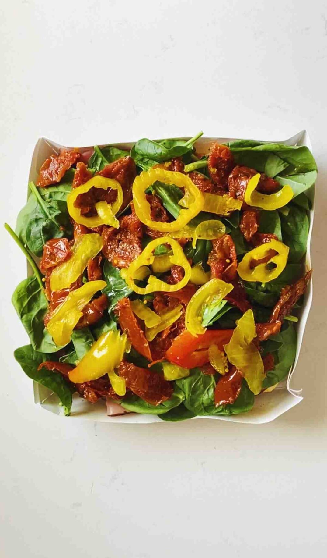 antipasto ingredients like yellow banana peppers, sun dried tomatoes and green spinach on top of slider buns. .