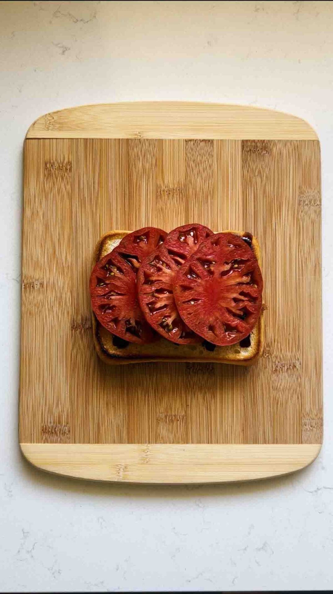 3 slices of fresh heirloom tomatoes that are dark red on a cutting board.