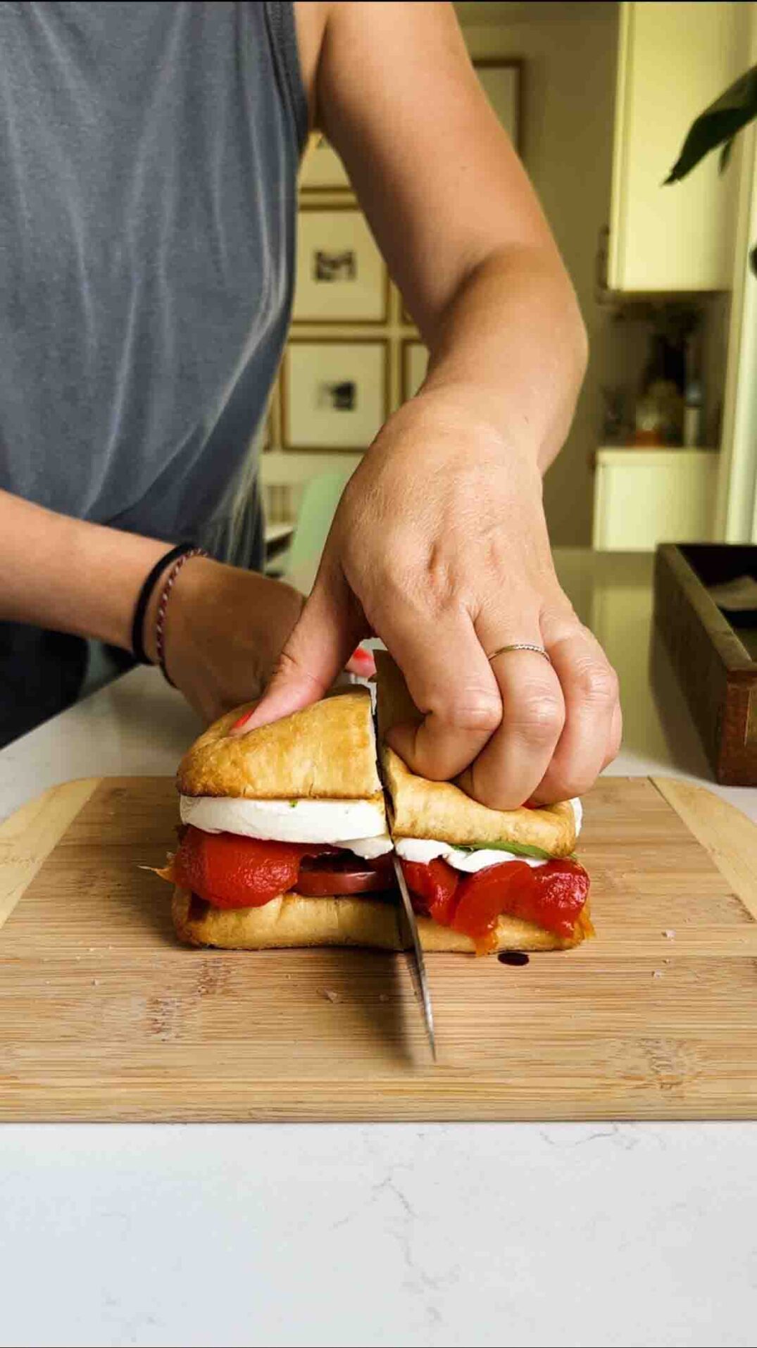 a hand cutting a caprese sandwich in half on a cutting board.