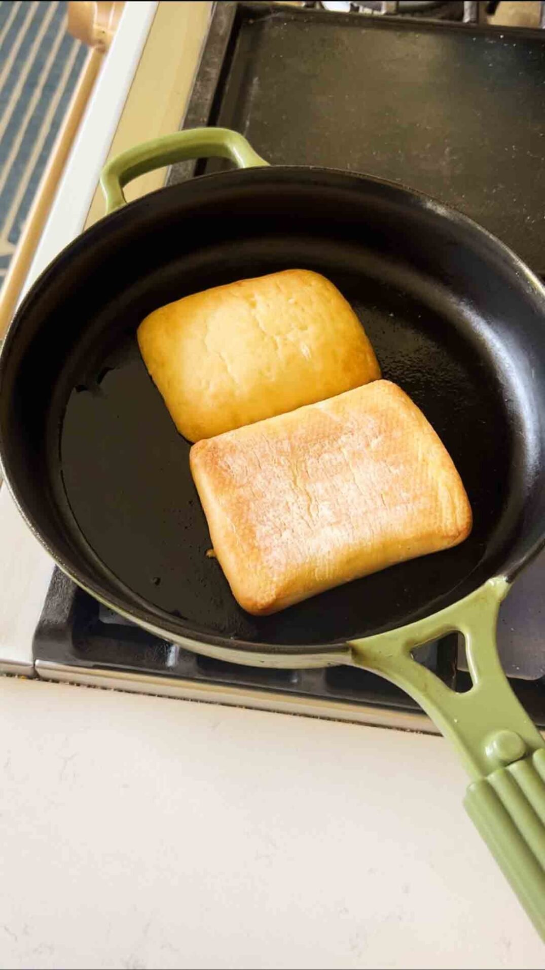 ciabatta bread toasting in a green cast iron skillet.