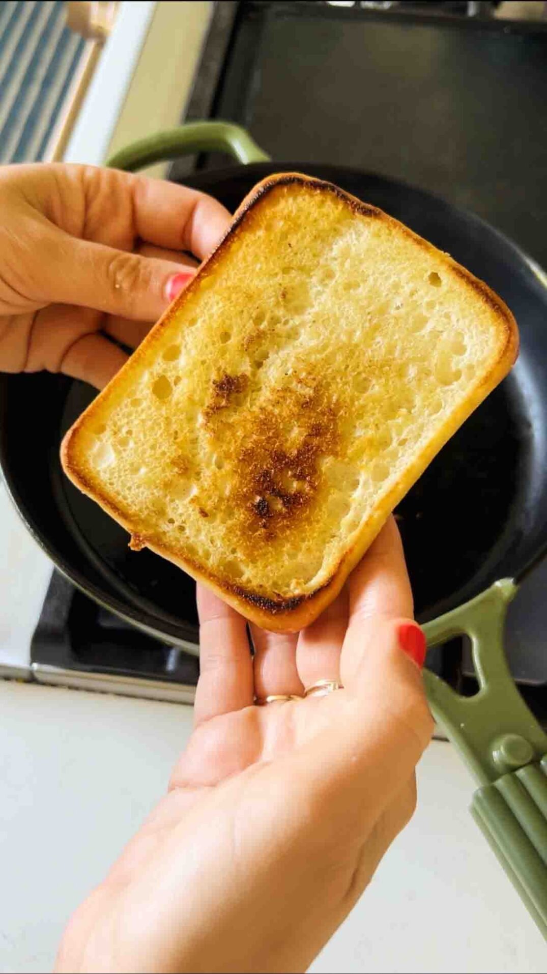a hand holding toasted ciabatta bread over a green cast iron skillet.