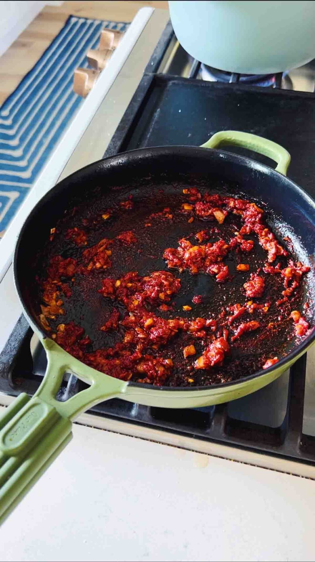 tomato paste in a green cast iron skillet on the stovetop.