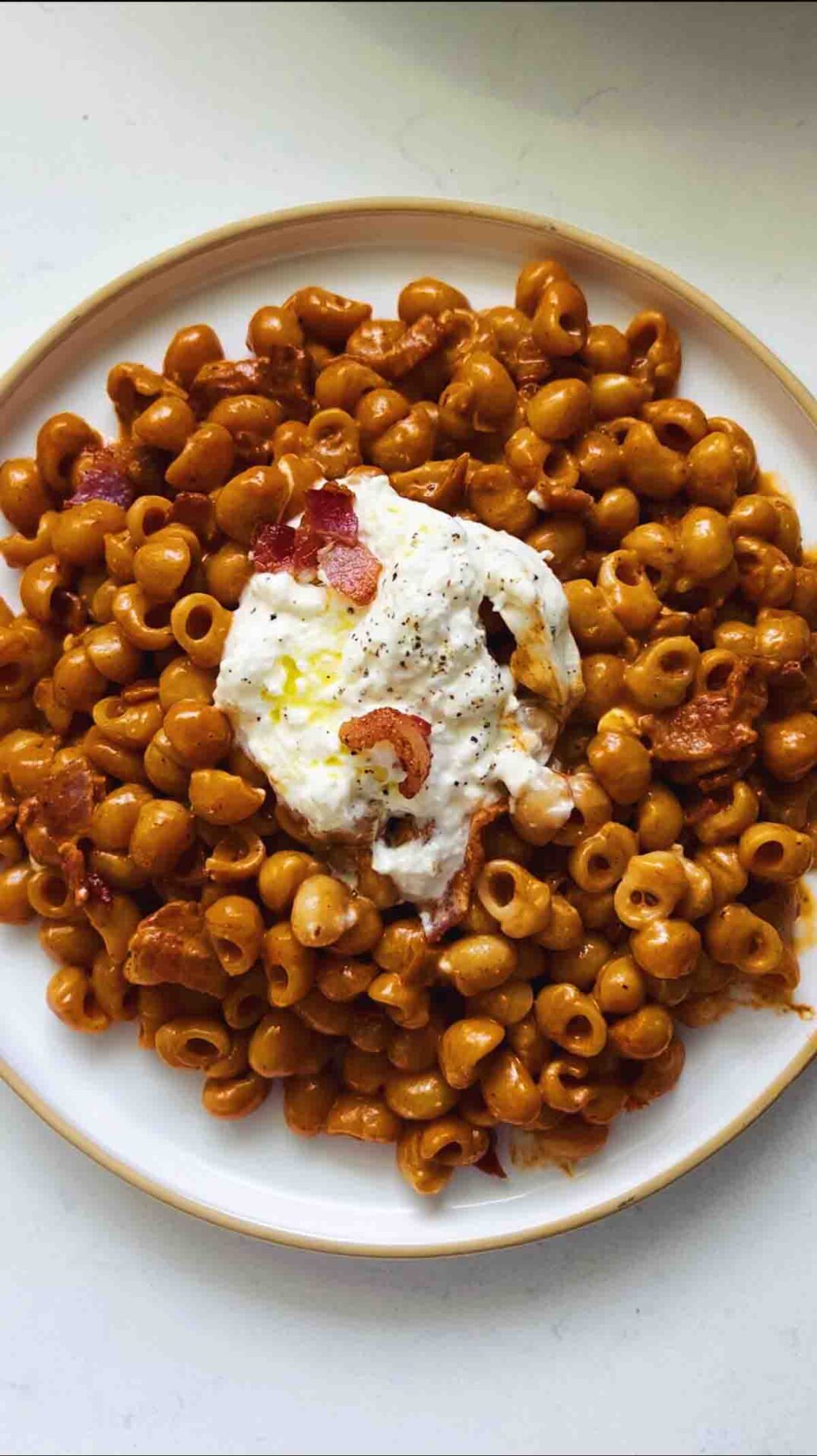 a plate full of spicy vodka pasta topped with bacon and burrata on a white surface.