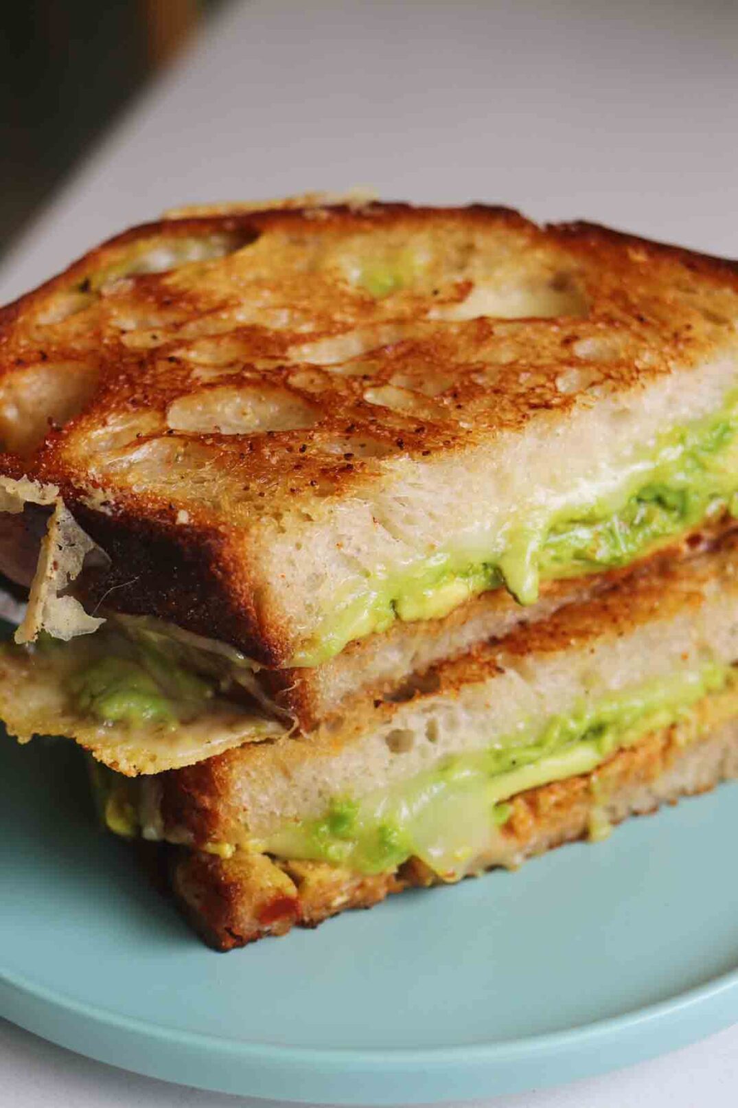 crusty golden bread with oozing cheese and green avocado on a blue plate.