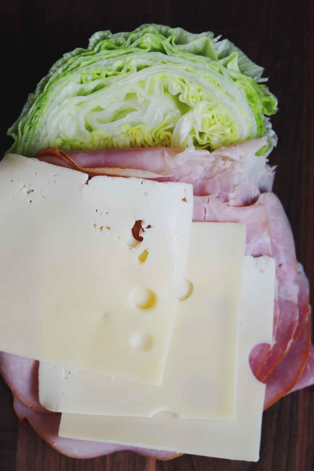 lettuce, ham, swiss cheese on a dark wooden cutting board.