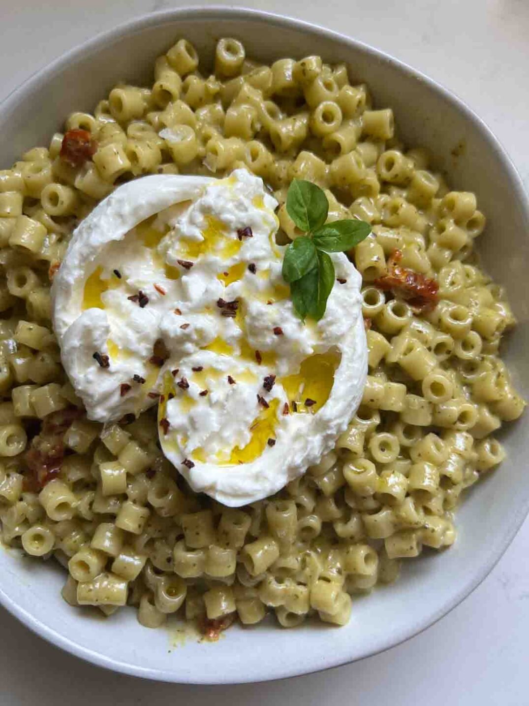 up close of a creamy pesto pasta in a white bowl with a ball of burrata on top.