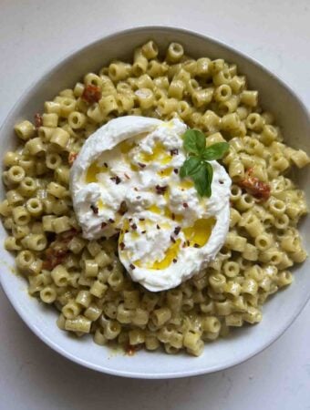 creamy pesto pasta in a white bowl with a ball of burrata on top.