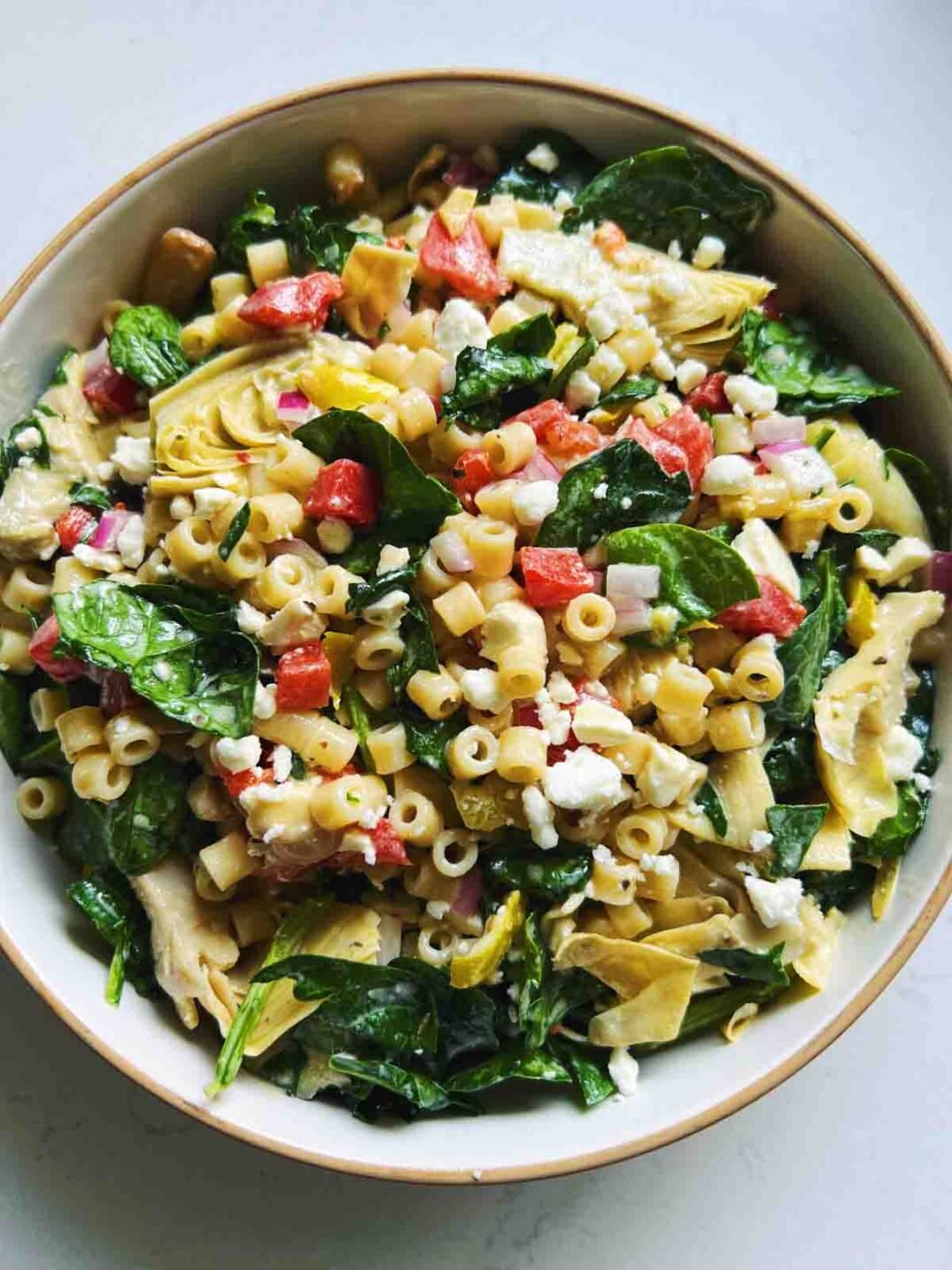 pulled back image of ditalini pasta salad with chopped veggies in a white bowl on a white countertop.