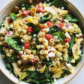 pulled back image of ditalini pasta salad with chopped veggies in a white bowl on a white countertop.