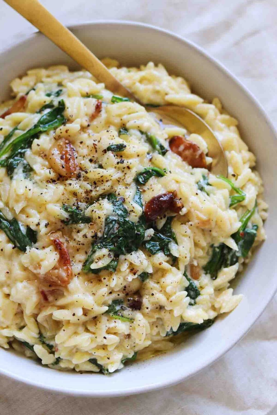 a golden spoon dipped into a bowl of creamy feta orzo with wilted spinach.
