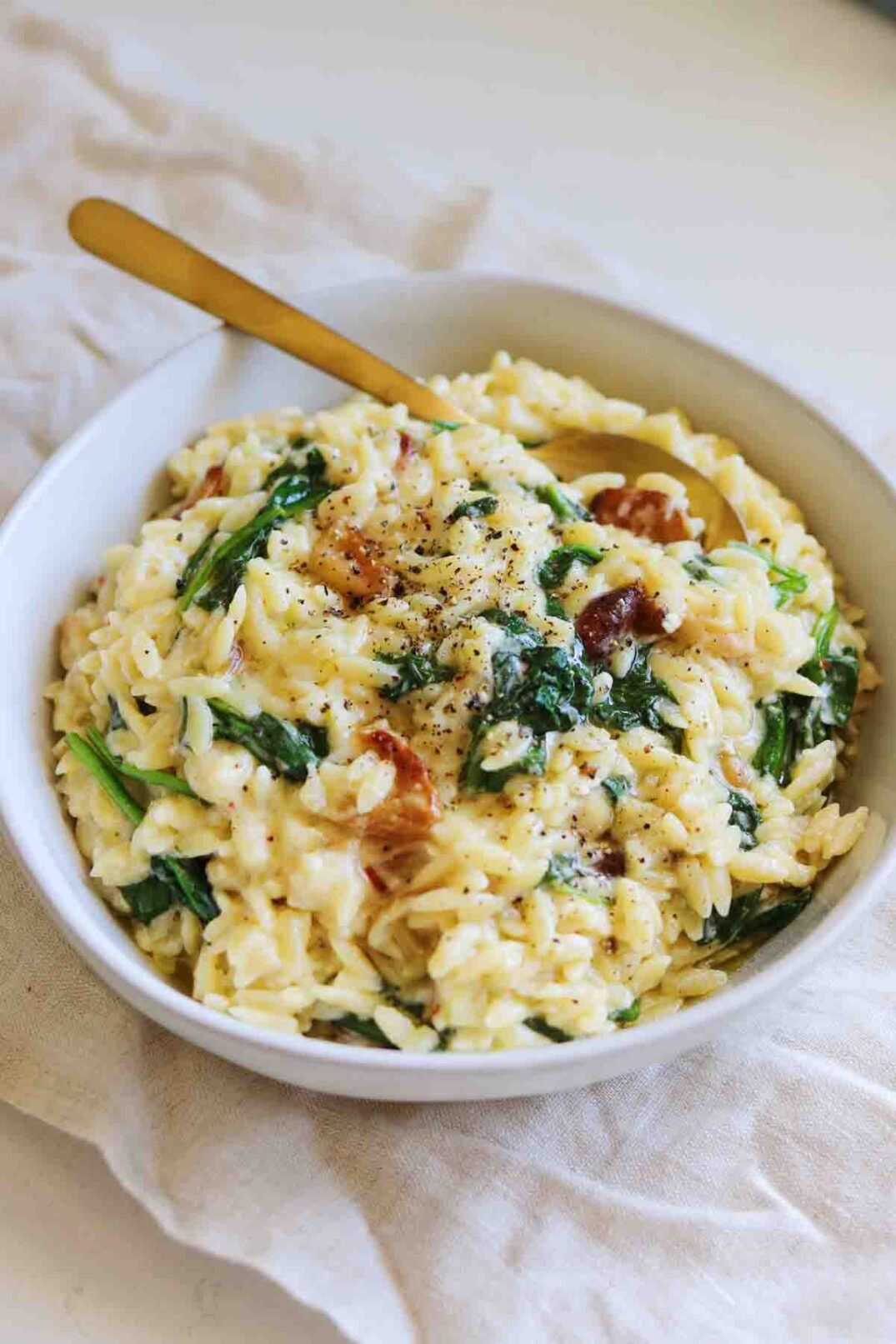creamy orzo in a white bowl with spinach and garlic on a white tablecloth.
