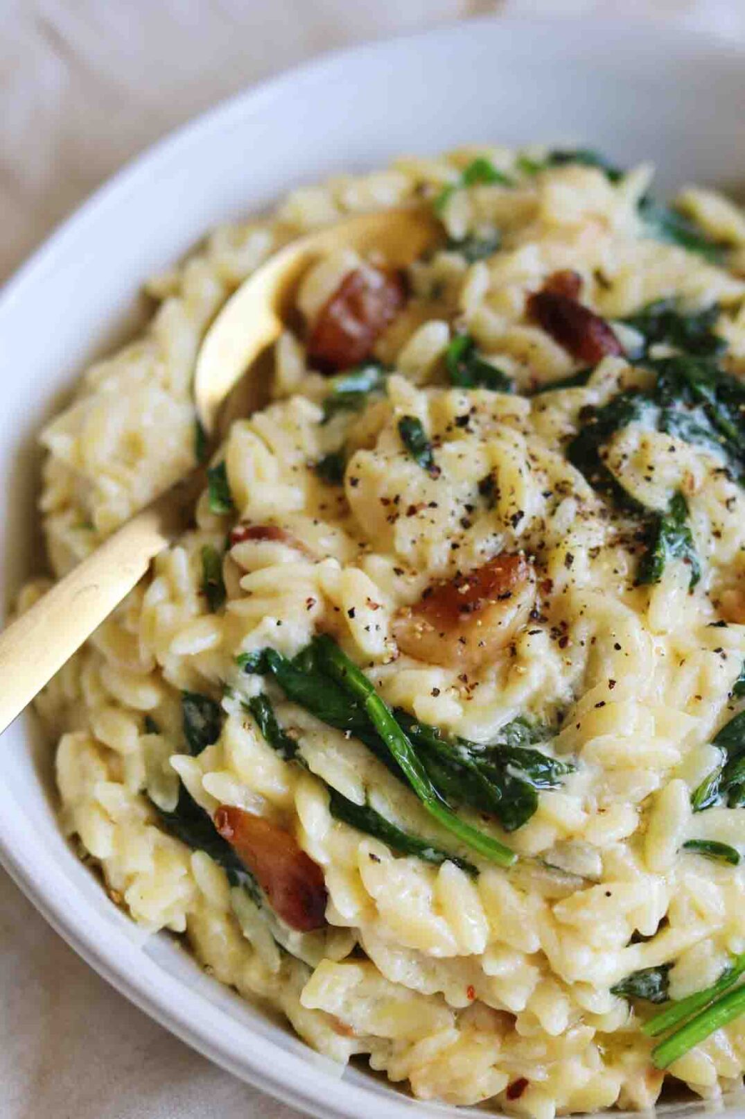 wilted spinach, golden roasted garlic cloves and creamy orzo in a white bowl.