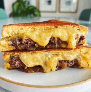 melted cheese oozing out of a truffle smash burger grilled cheese on a white plate.