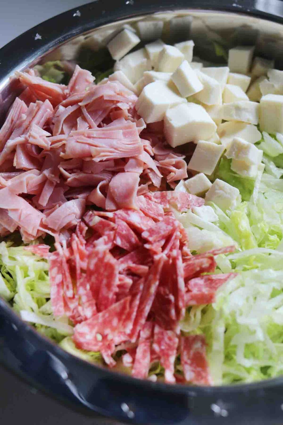 chopped up italian cold cuts in a silver bowl with shredded lettuce.