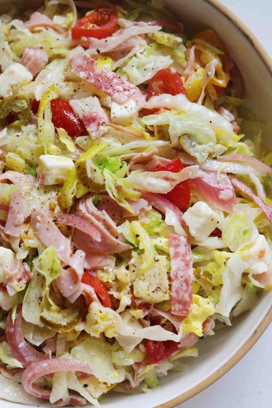a close up of colorful chopped veggies and cold cuts in a white bowl.